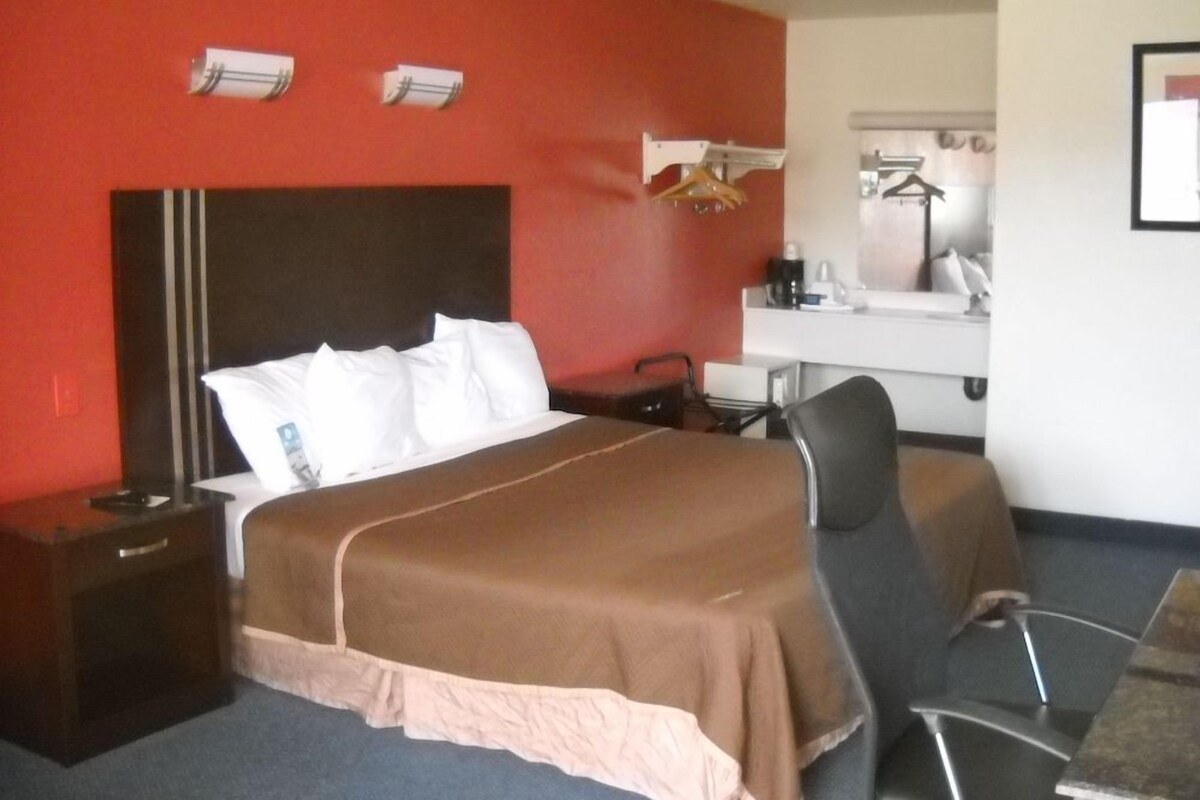 A hotel room with a bed, a desk, a chair, and a mirror.