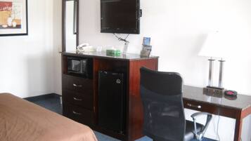 Een hotelkamer met een bed, een bureau met een computer, een stoel, een televisie, een magnetron en een koelkast.