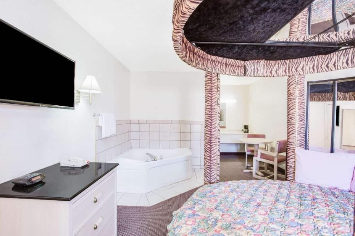 A hotel room with a bed, a desk, a chair, a bathtub, and a TV.