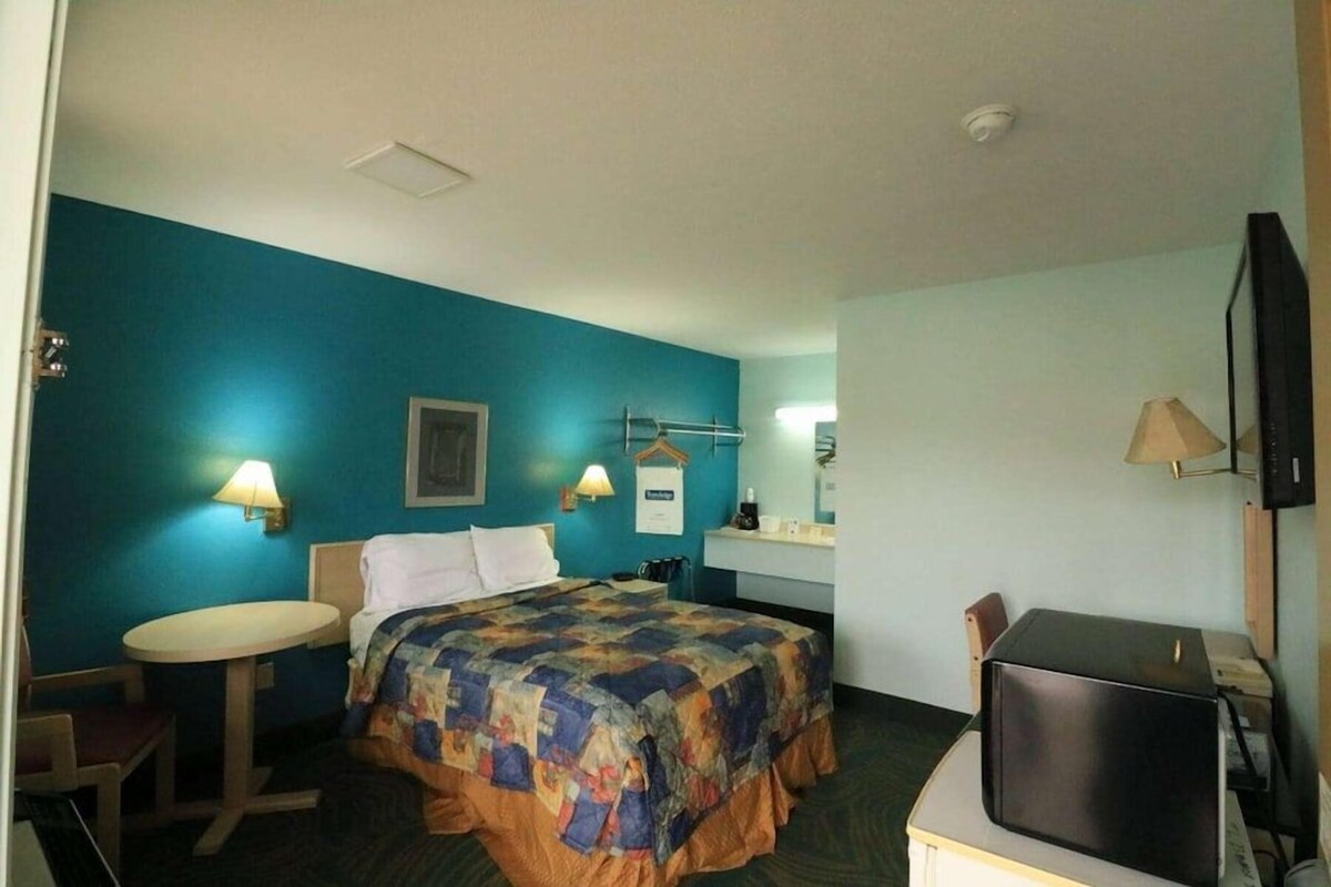 A hotel room with a bed, a desk, a chair, a television, and a small table.