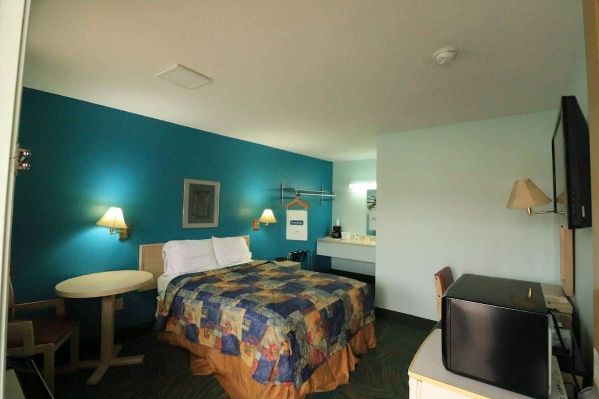A hotel room with a bed, a desk, a chair, a TV, and a small table.