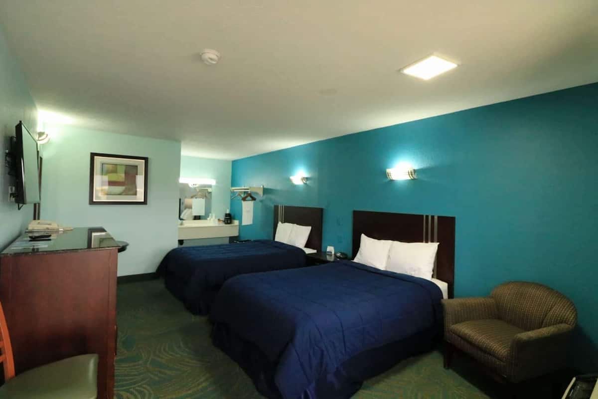 A hotel room with two beds, a desk, a chair, a mirror, and a framed picture on the wall.