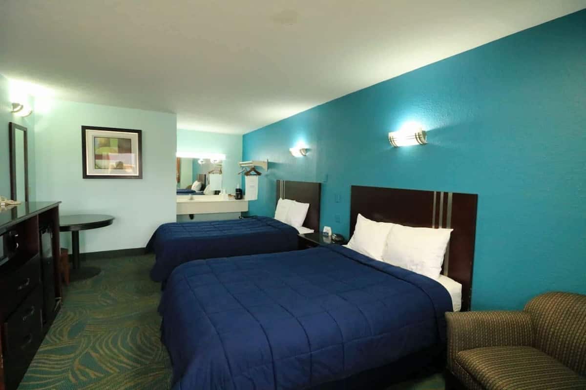 A hotel room with two beds, a desk, and a chair.