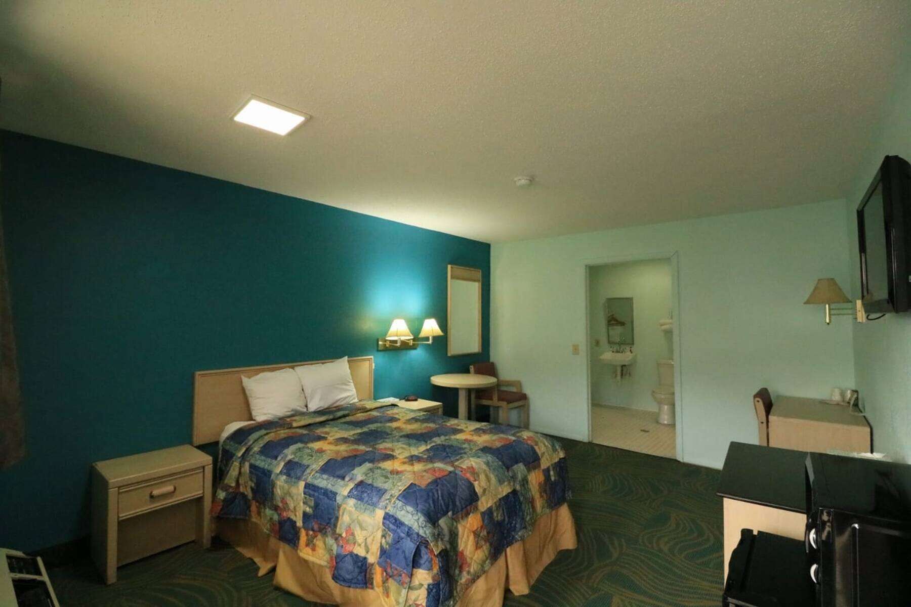 A hotel room with a bed, bedside table, lamp, and a small round table.