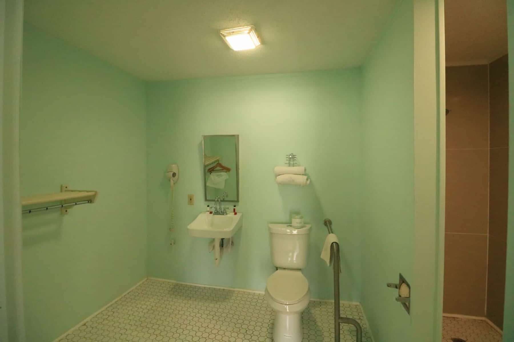 A bathroom with a toilet, sink, and mirror. There is a towel rack above the sink and a shower area to the right.