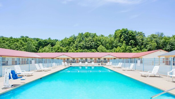 Piscina com espreguiçadeiras e um edifício com telhado vermelho ao fundo.