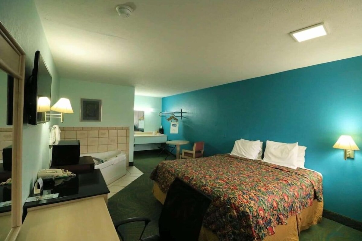 A hotel room with a bed, desk, chair, and a bathroom visible in the background.