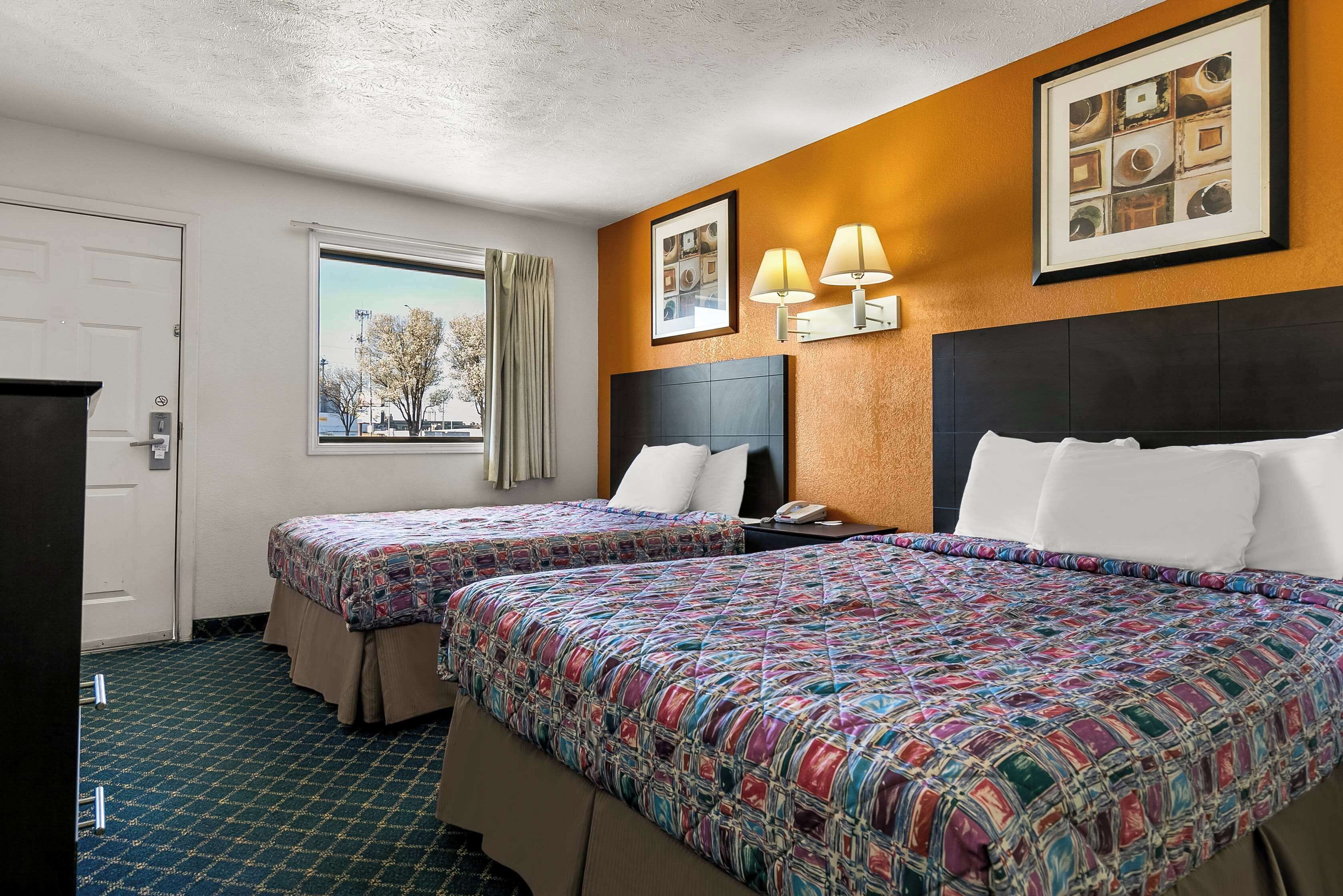 A hotel room with two beds, a window with a view, a door, and a framed picture on the wall.