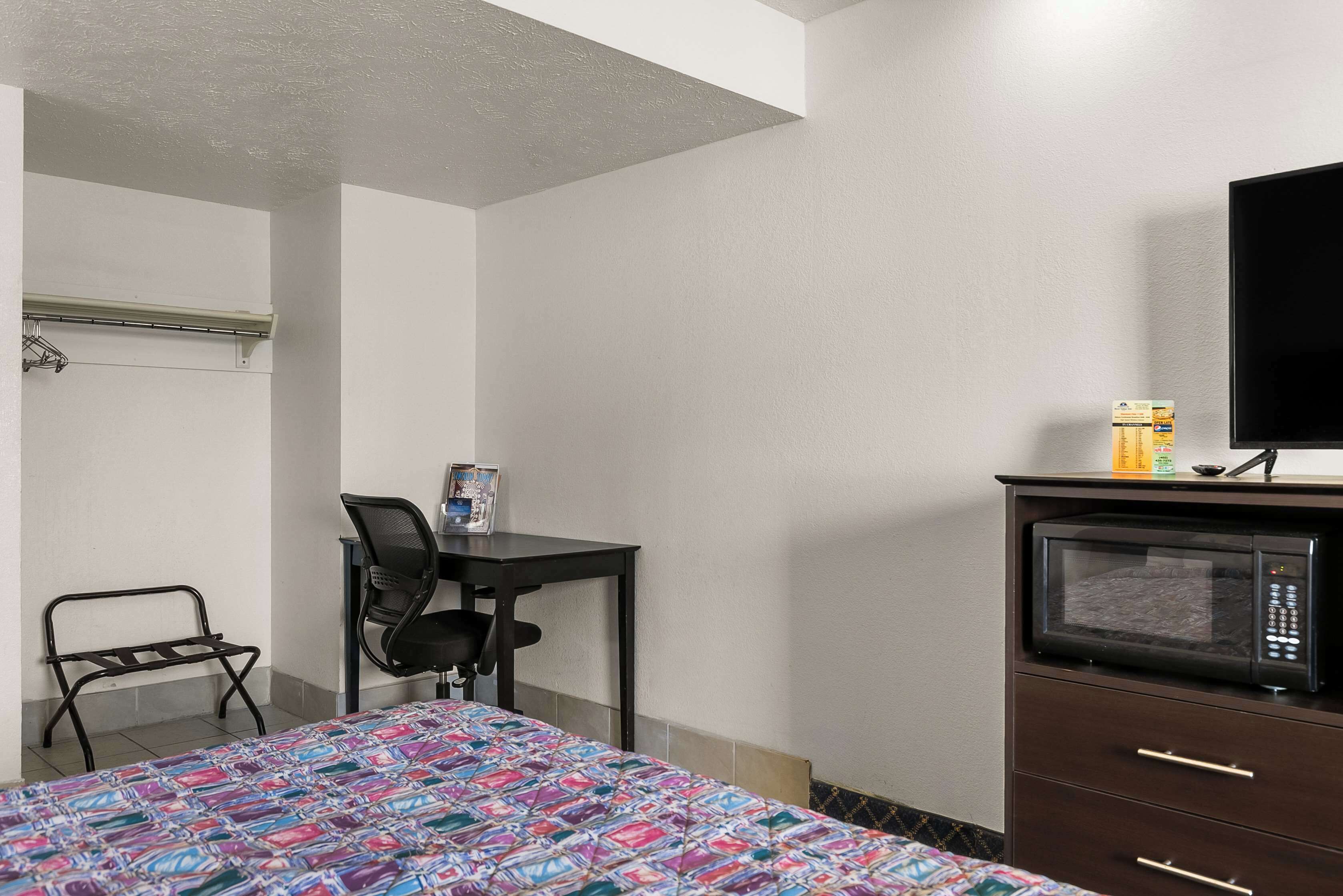 A hotel room with a bed, a desk with a chair, a microwave, and a TV on a dresser.