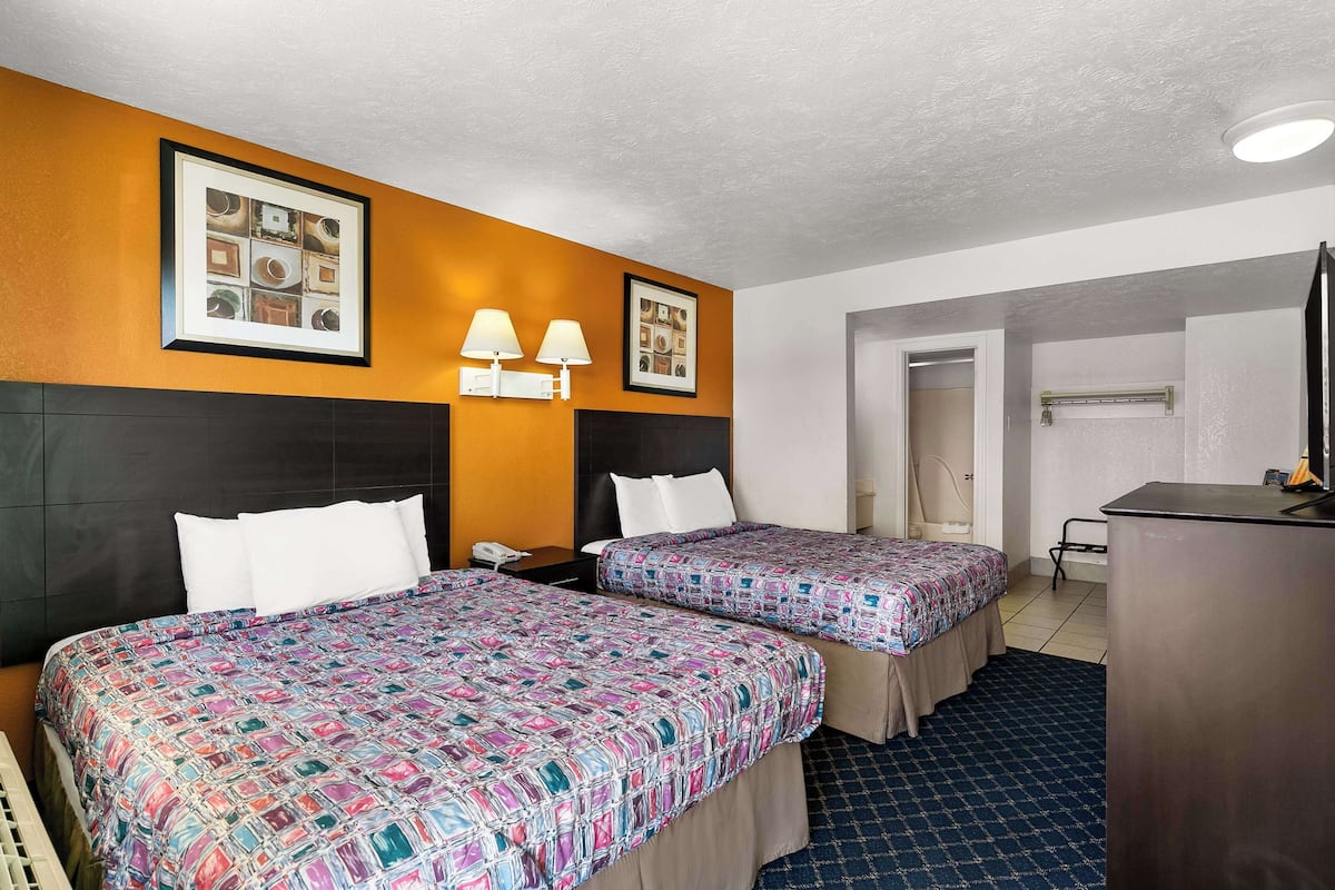 A hotel room with two beds, a desk, a phone, and framed pictures on the wall.