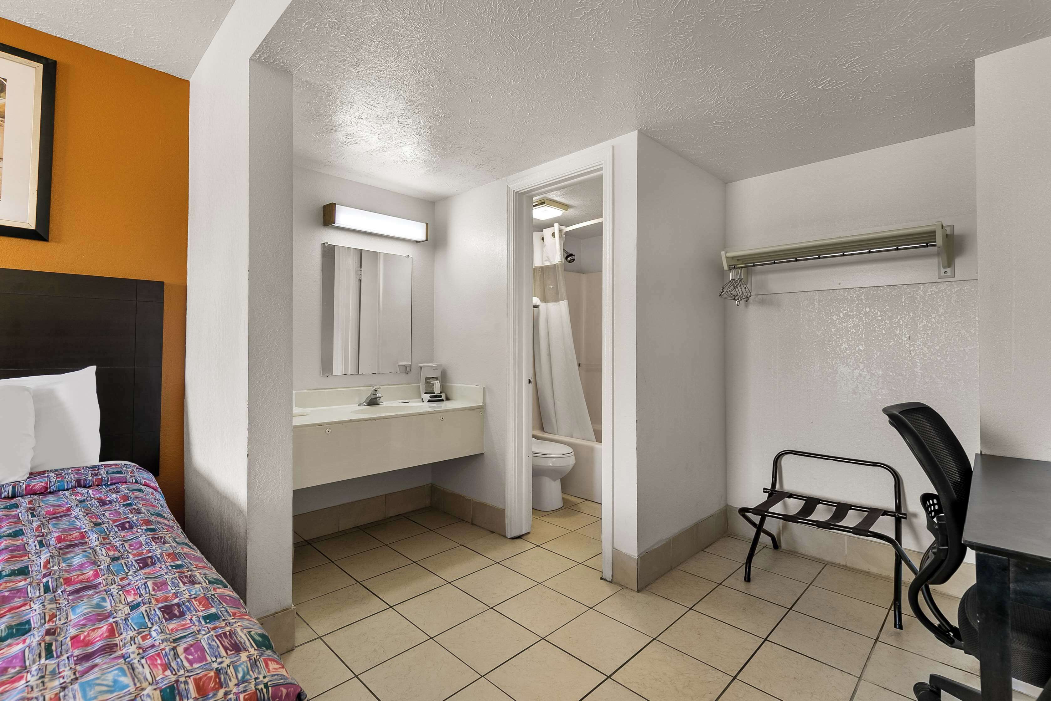 A hotel room with a bed, a bathroom with a toilet and sink, and a chair.