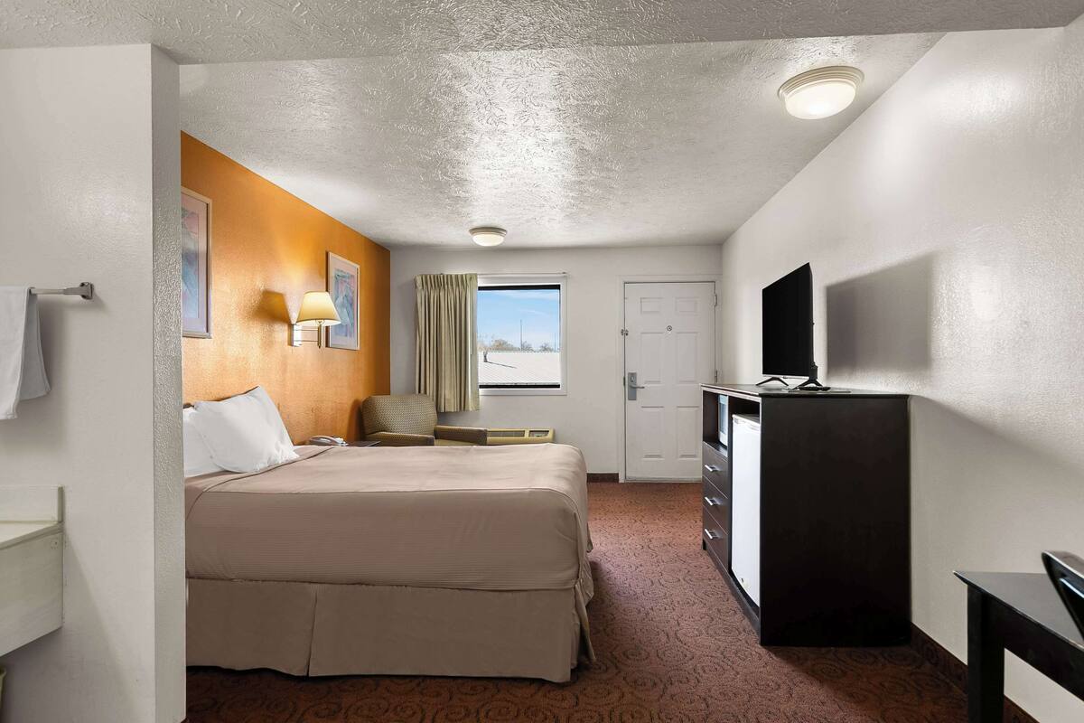 A hotel room with a bed, a desk, a television, a window with a view, and a door.