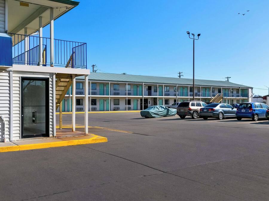A motel with a two-story structure, a covered parking area, and a clear blue sky.