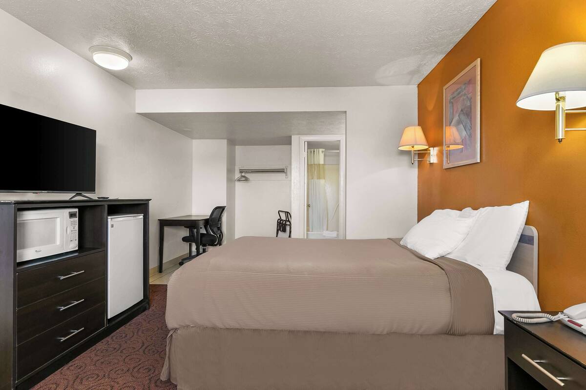 A hotel room with a bed, a desk with a chair, a microwave, and a refrigerator.