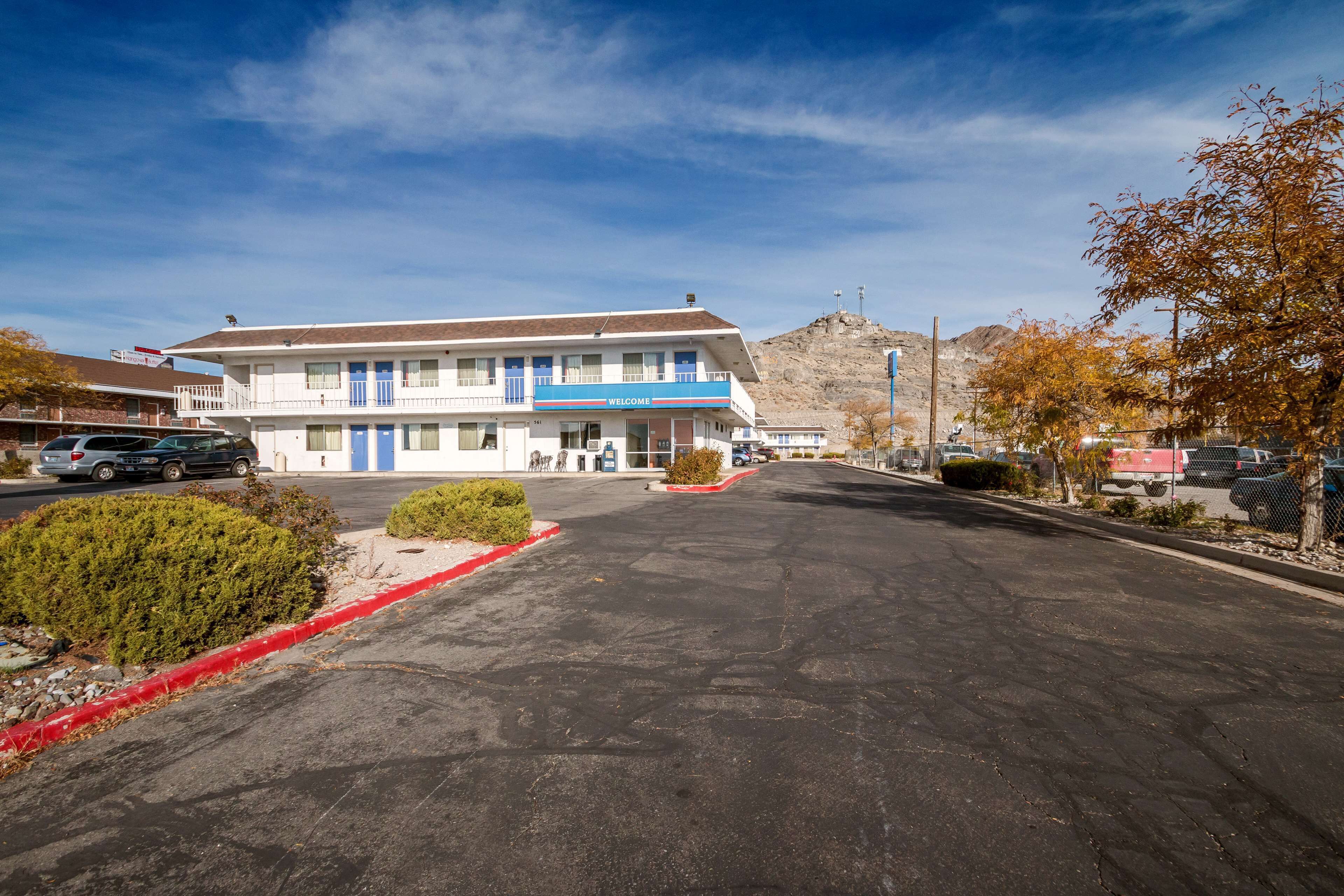 A motel with a 'WELCOME' sign, a parking lot, and a mountain in the background.