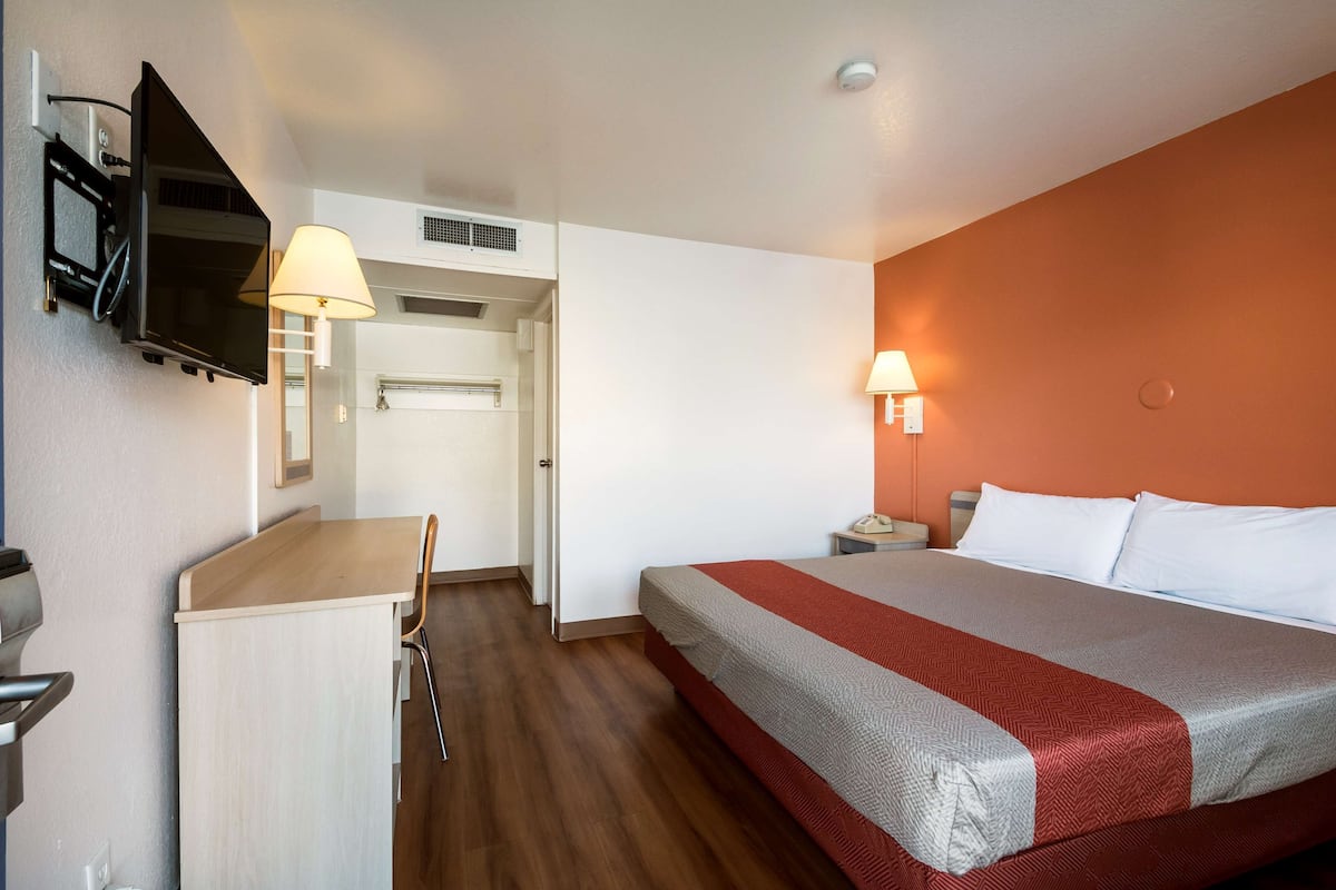 A hotel room with a bed, desk, chair, and a TV mounted on the wall.