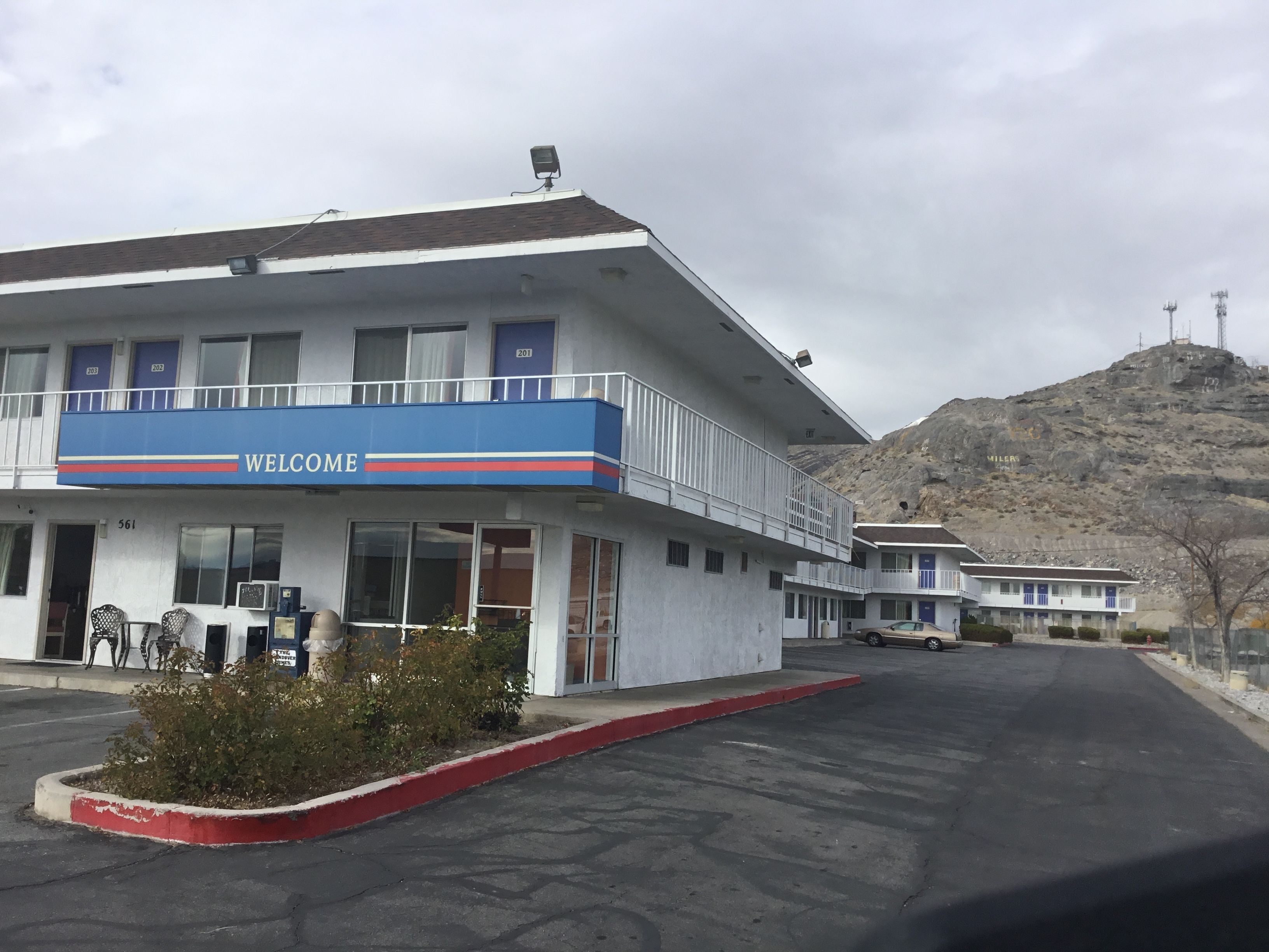 A motel with a 'WELCOME' sign, a parking lot, and a mountainous backdrop.
