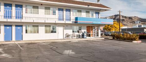 A motel with a blue 'Welcome' sign, multiple rooms, a parking lot, and a mountain in the background.