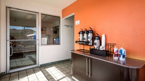 Un espace d’accueil d’hôtel doté d’une entrée avec une porte en verre, d’un comptoir avec des machines à café et de distributeurs automatiques.