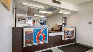 Un comptoir d’accueil de motel avec un grand panneau indiquant le chiffre « 6 », une photo encadrée d’un canyon et un panneau sur lequel on peut lire : « Nous laisserons la lumière allumée pour vous. »