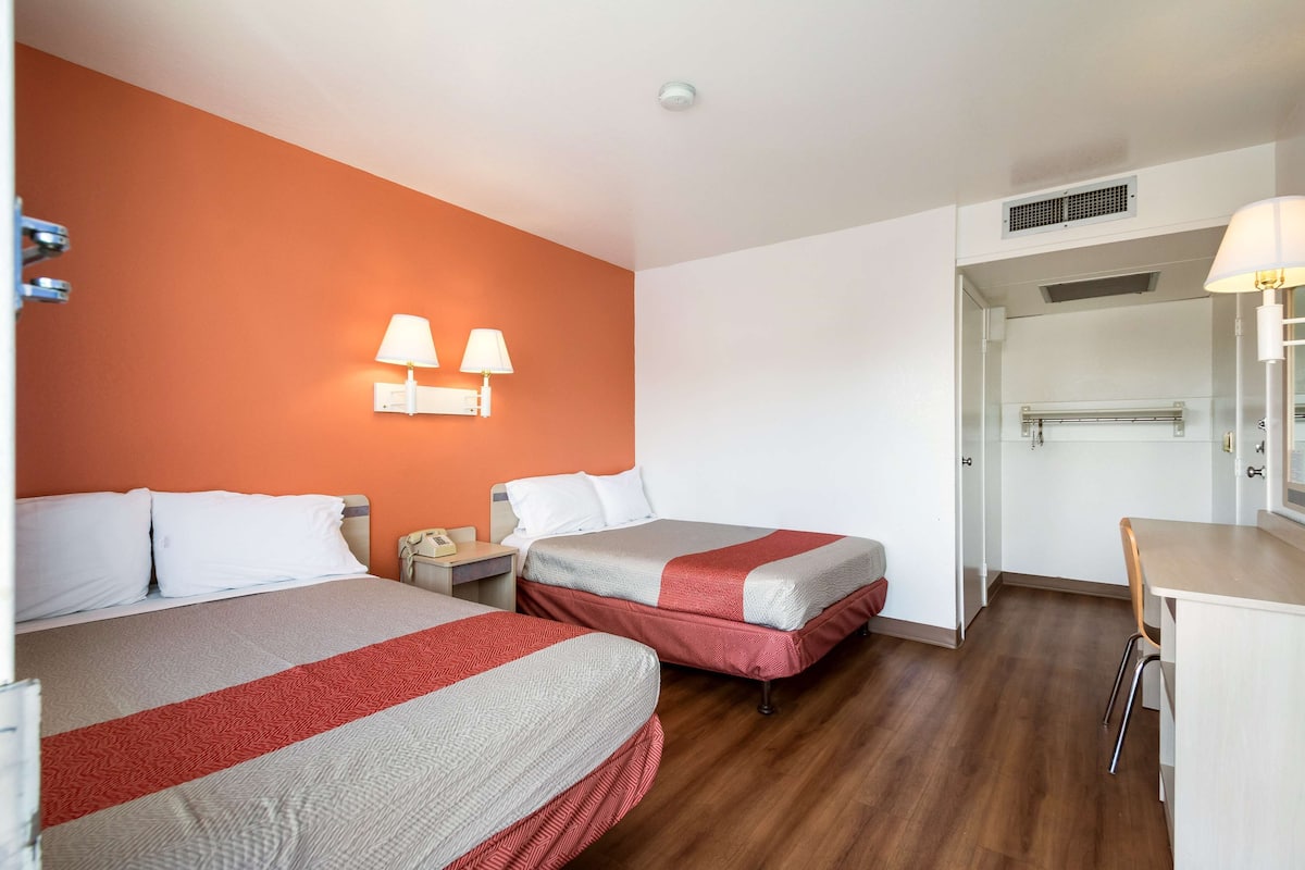 A hotel room with two beds, a desk, a chair, a wardrobe, and a bathroom.