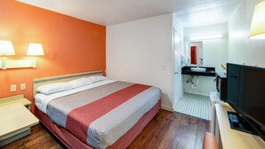 A hotel room with a bed, bedside tables, a TV, a bathroom with a sink and mirror, and a red curtain.