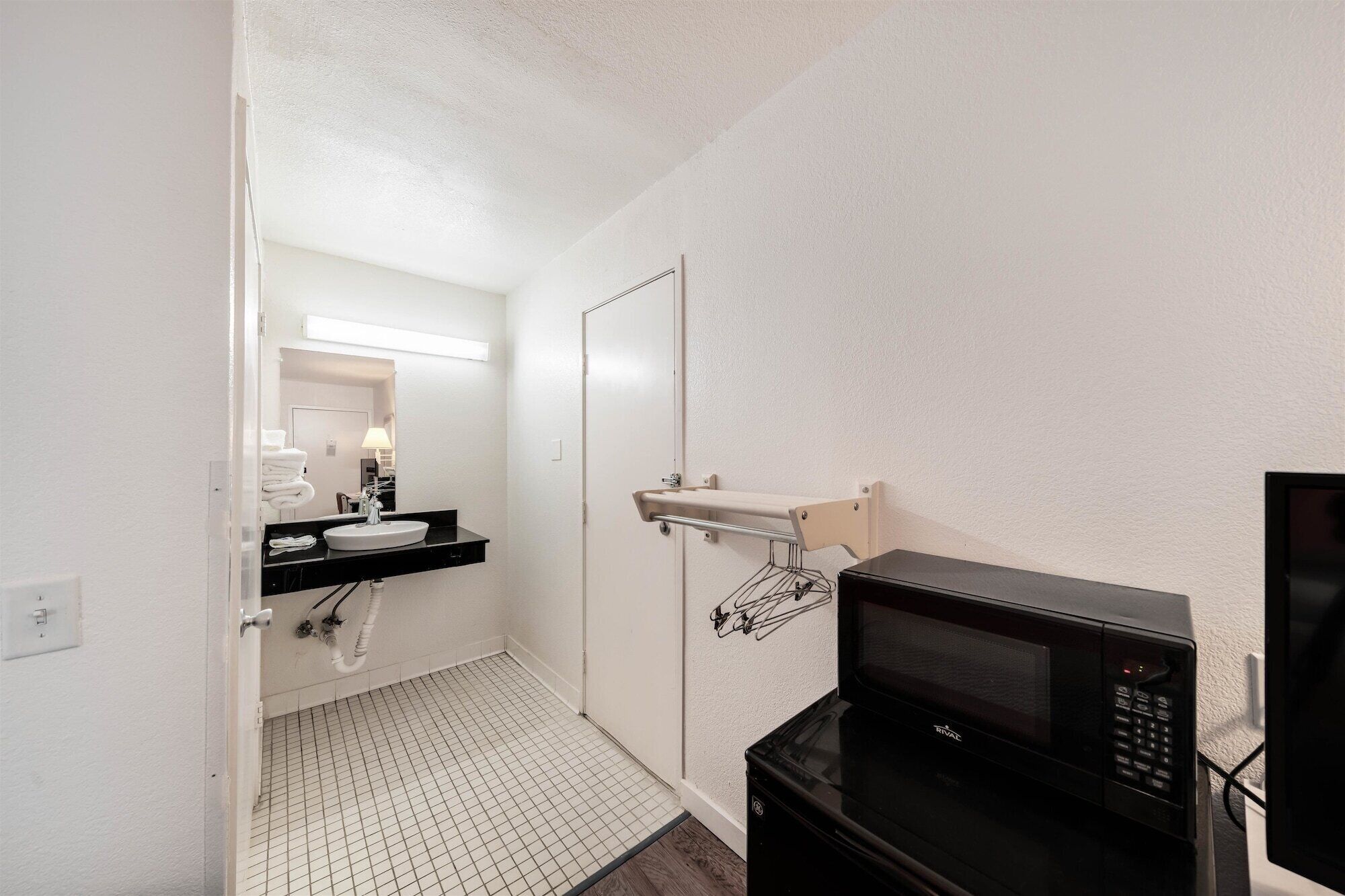 Een kleine badkamer met een wit wastafel, een spiegel, een handdoekhouder, een magnetron en een vloer met een ruitpatroon.