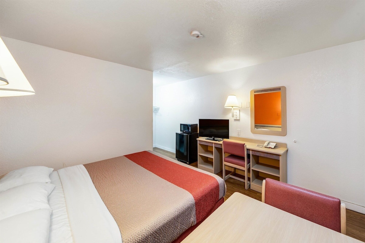 Een hotelkamer met twee bedden, een bureau met een computer en telefoon, een televisie en een kleine koelkast.