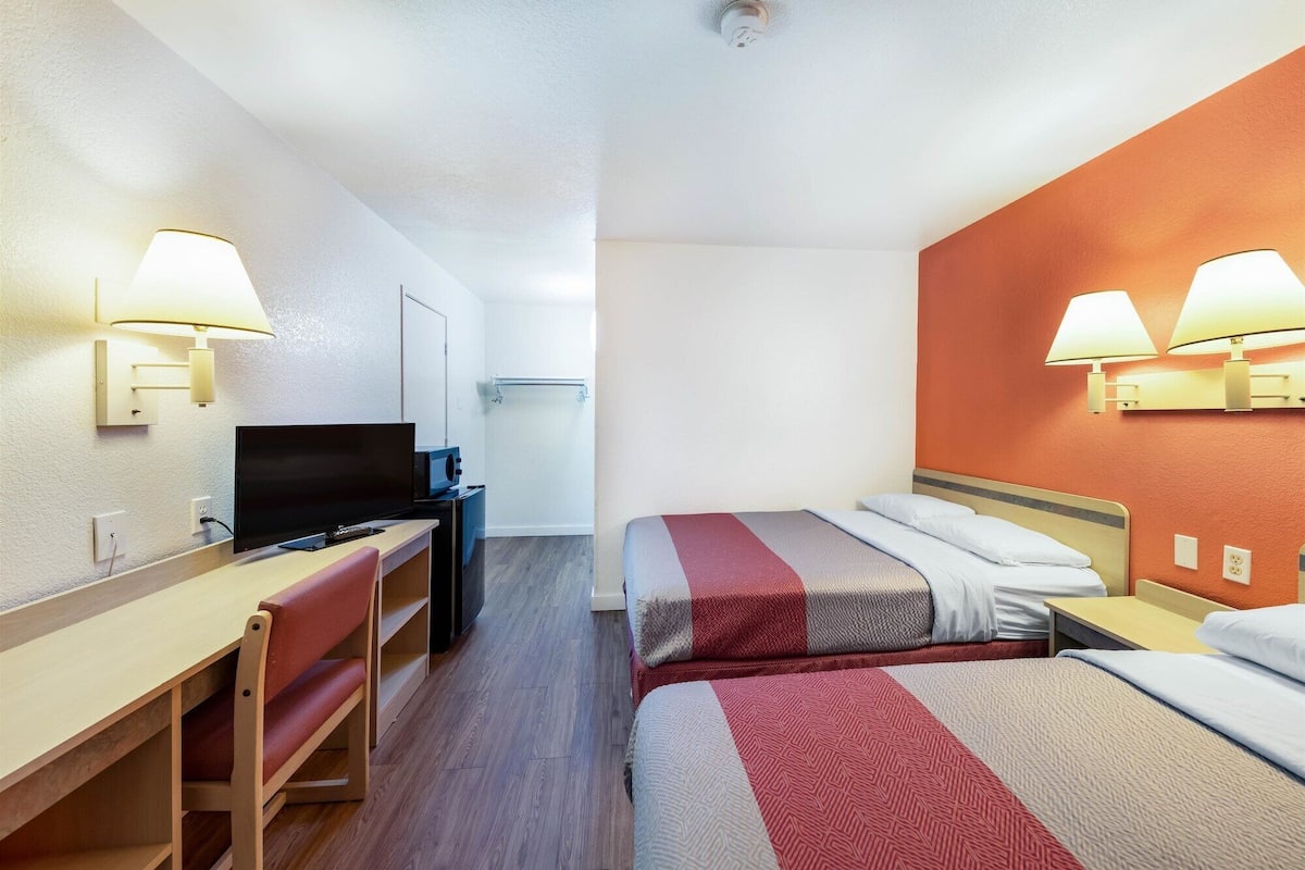 Een hotelkamer met een bureau, televisie, twee bedden en wandlampen.