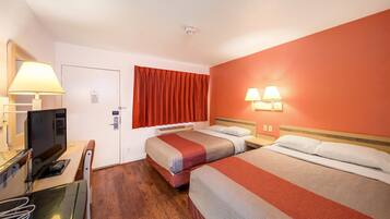 Habitación de hotel con dos camas, un escritorio con computadora, un televisor y una ventana con cortinas rojas.