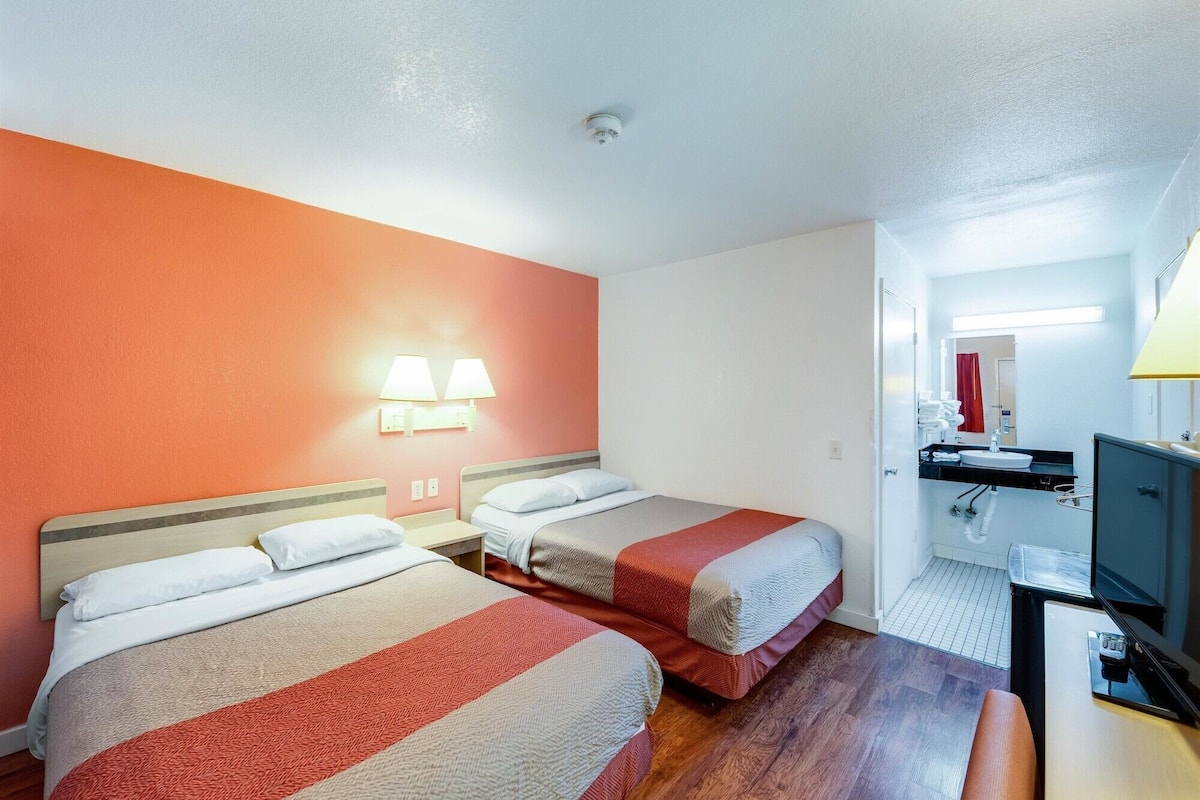 Een hotelkamer met twee bedden, een bureau, een televisie en een badkamer zichtbaar door een geopende deur.