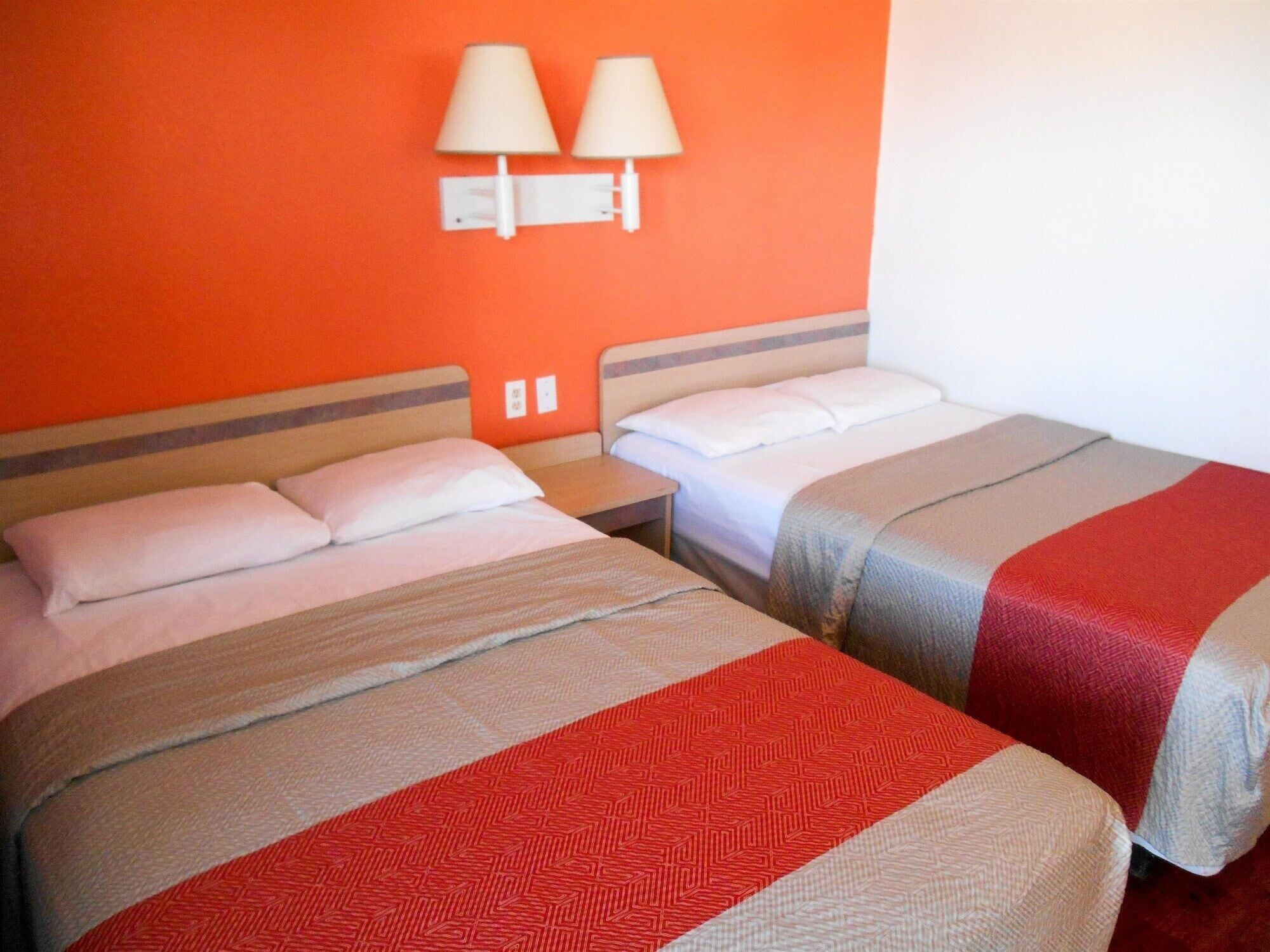 A hotel room with two beds, each with a different patterned bedspread. There are two wall-mounted lamps above the beds.