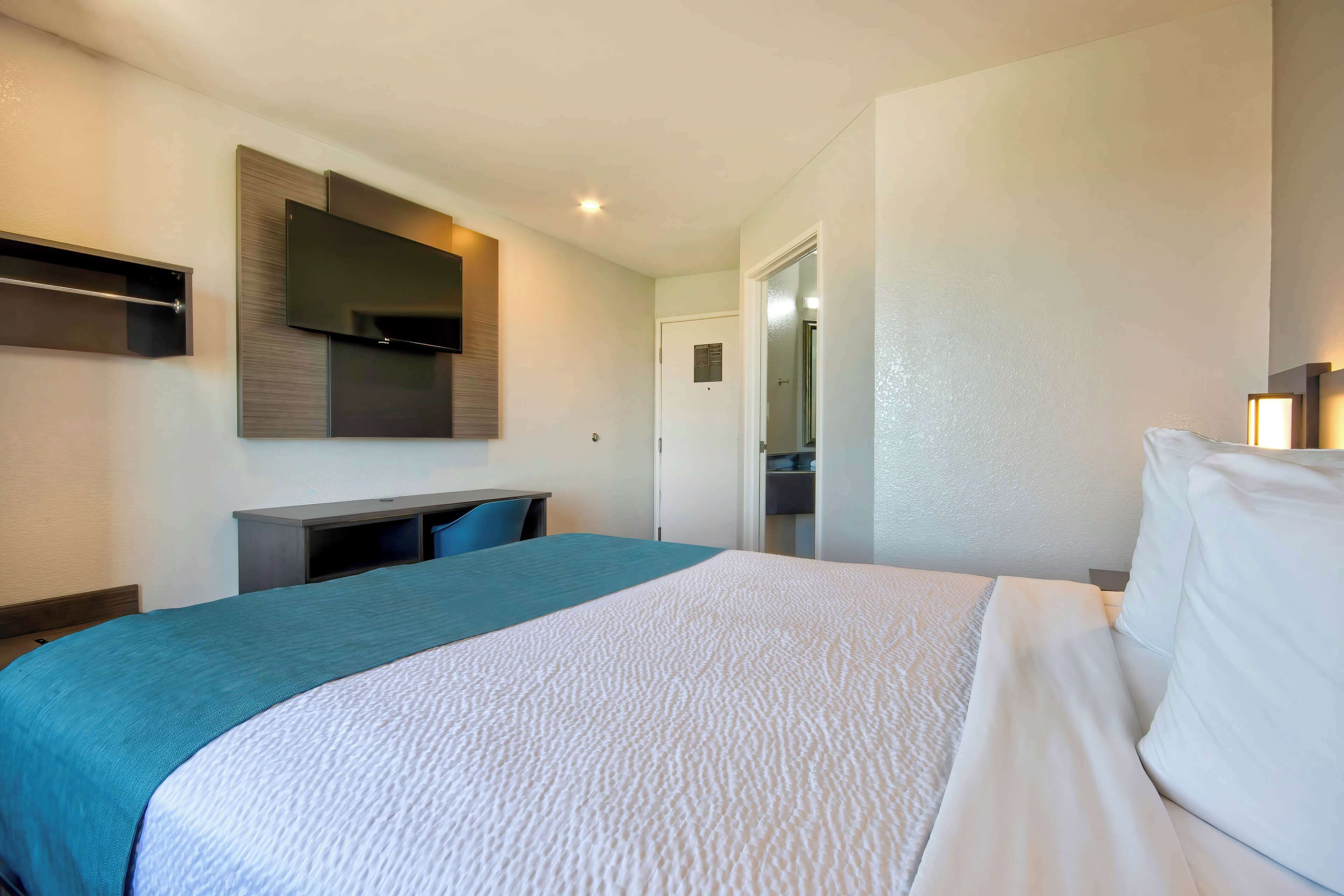 Habitación de hotel con cama, escritorio, televisor de pantalla plana y puerta que da a un baño.
