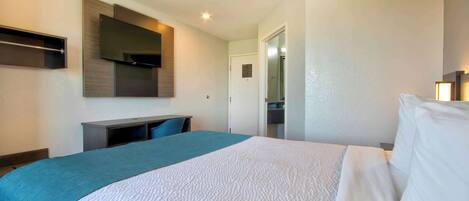 A hotel room with a bed, a desk, a flat-screen TV, and a door leading to a bathroom.