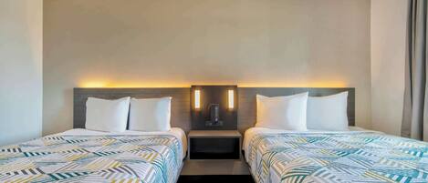 A hotel room with two beds, a nightstand with a lamp, and a wall-mounted light fixture.