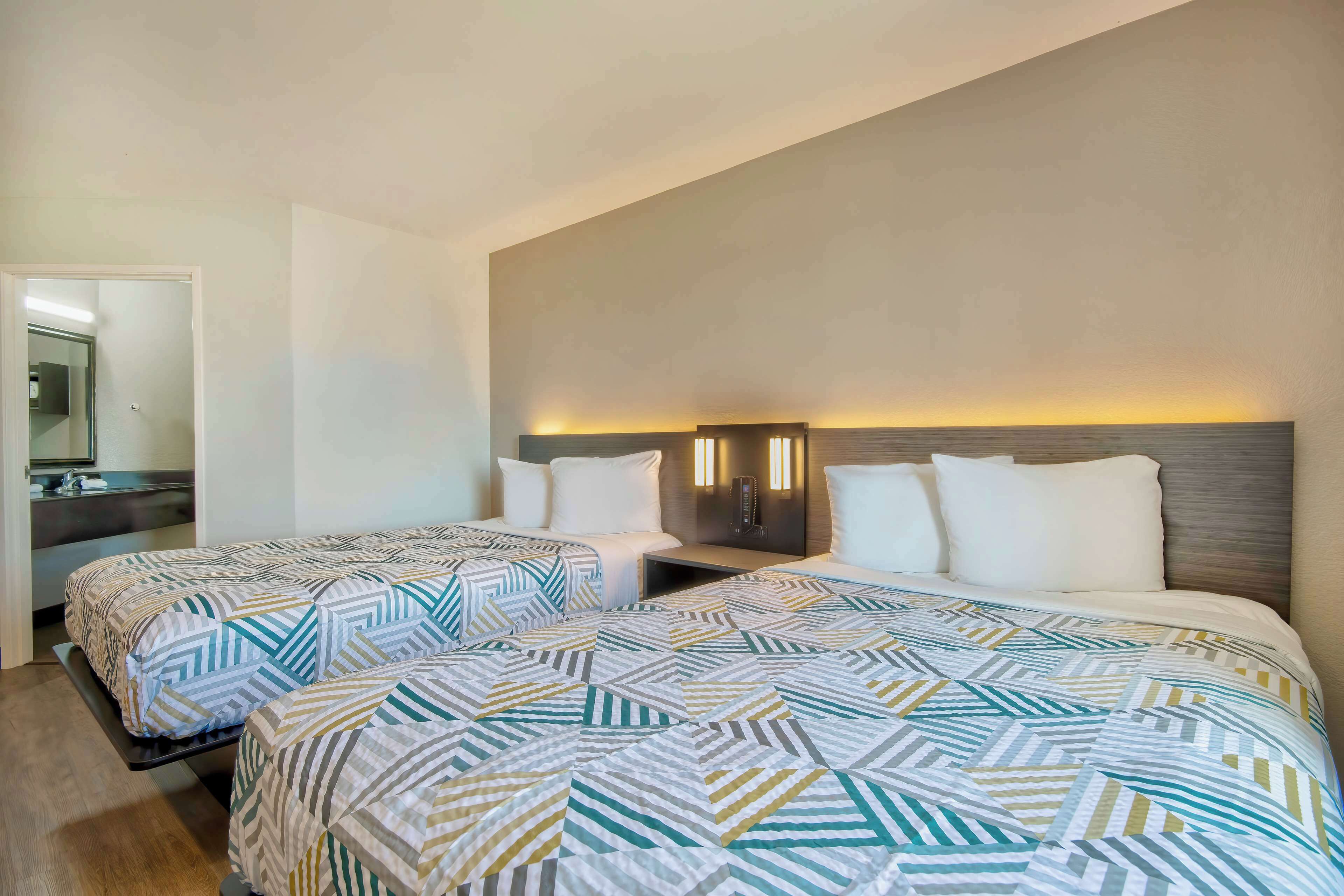 A hotel room with two beds, a nightstand, a mirror, and a wall-mounted light fixture.