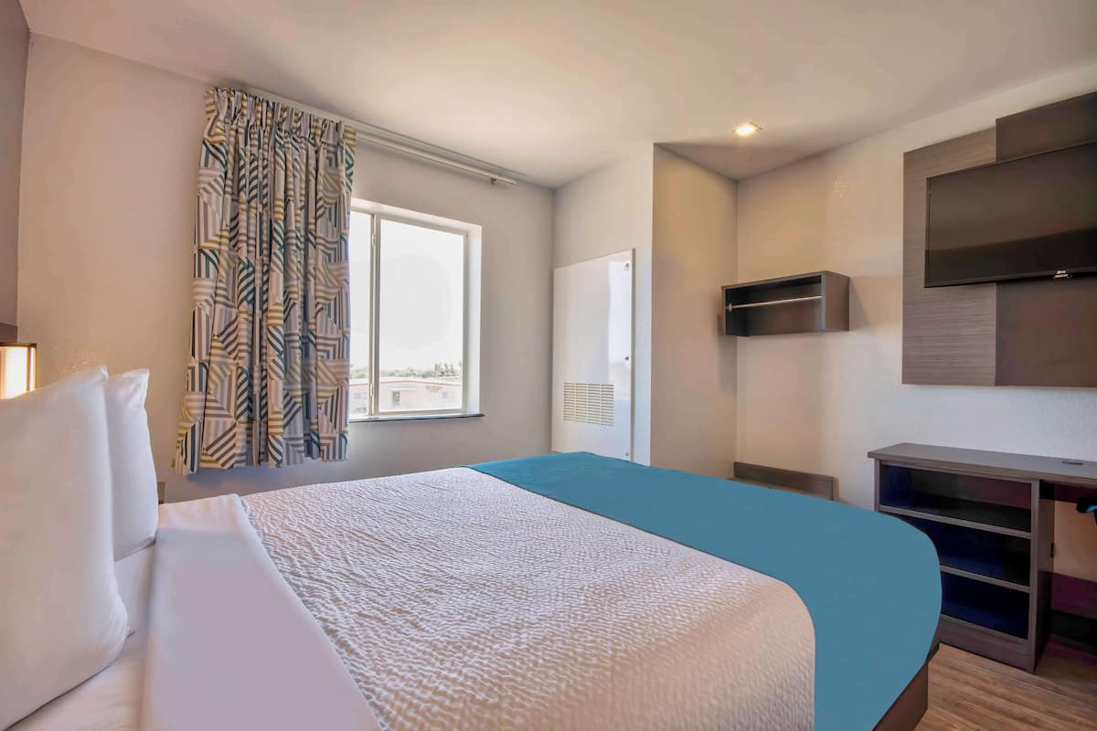 A hotel room with a large bed, a TV mounted on the wall, and a window with curtains.