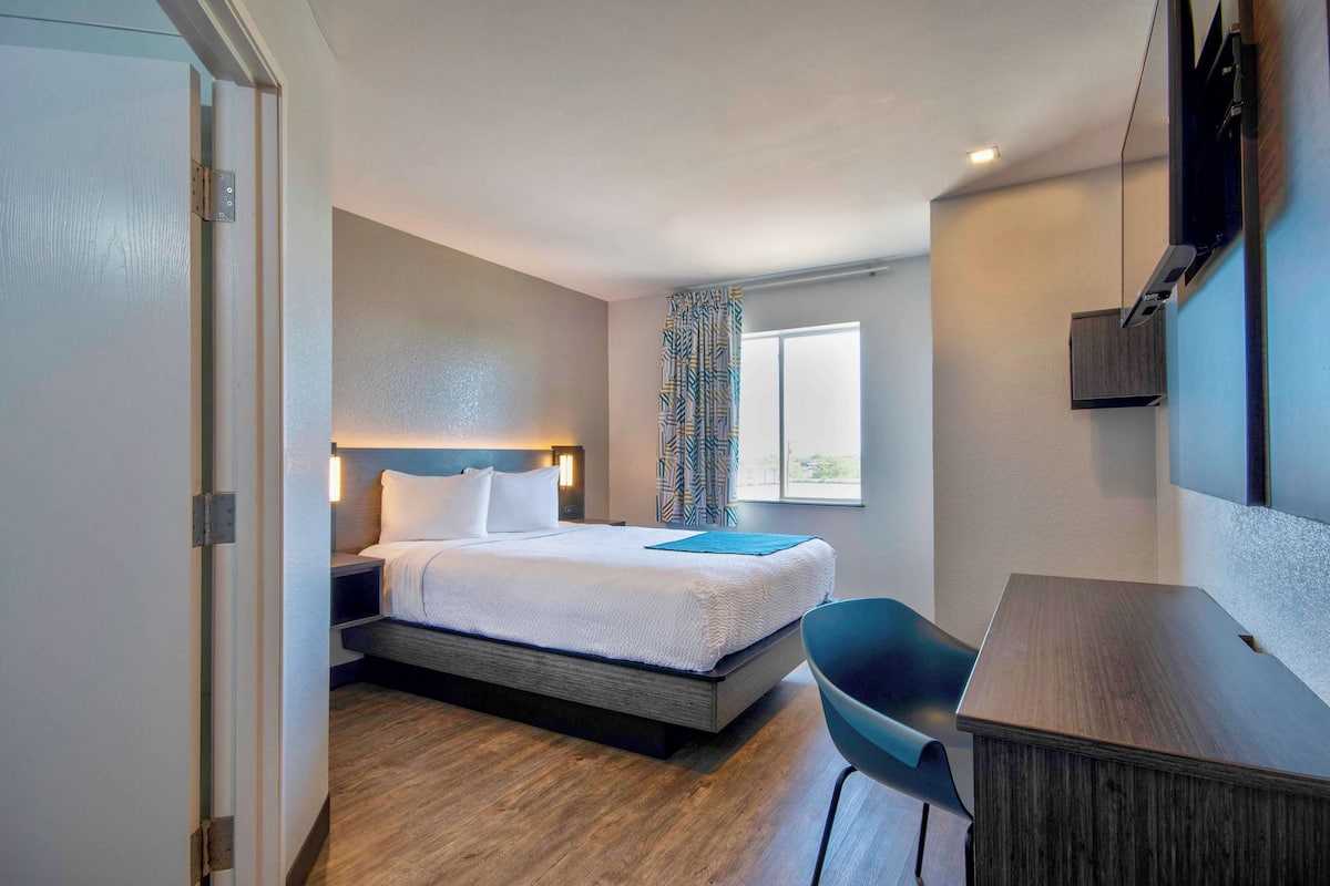 A hotel room with a bed, bedside table, chair, and a desk.