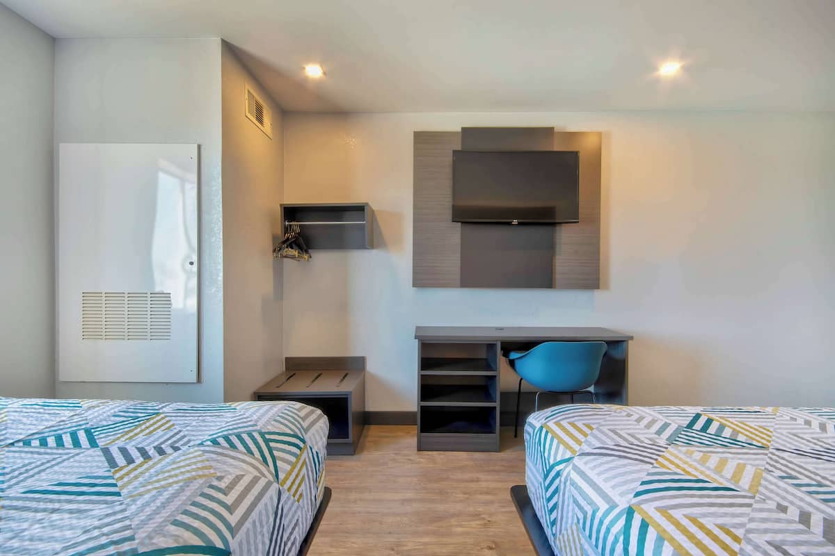 A hotel room with two beds, a desk, a chair, a TV, and a wardrobe.