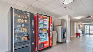 Zona con máquinas expendedoras, ofreciendo opciones de bocadillos y bebidas, un refrigerador de Coca-Cola y un bote de basura.