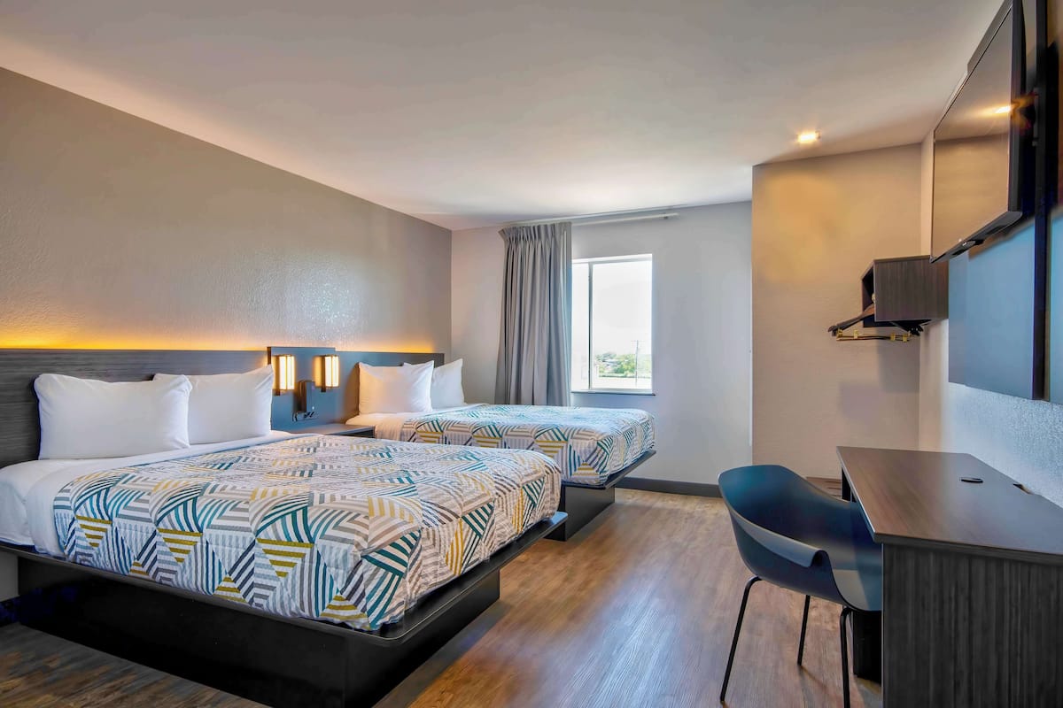 A hotel room with two beds, a desk, and a chair.