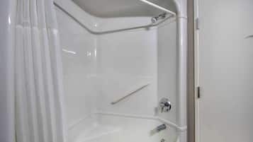 A corner shower with a white tub, a grab bar, and a door.