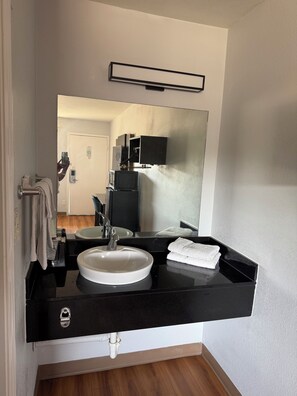 A modern bathroom with a black countertop, white sink, and a large mirror.