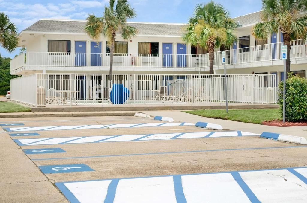 Um motel com estacionamento reservado para deficientes, cerca externa e um prédio de dois andares com sacadas.