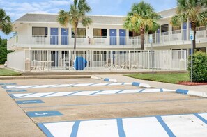 A motel with a parking lot marked for handicapped parking, a fenced exterior, and a two-story building with balconies.
