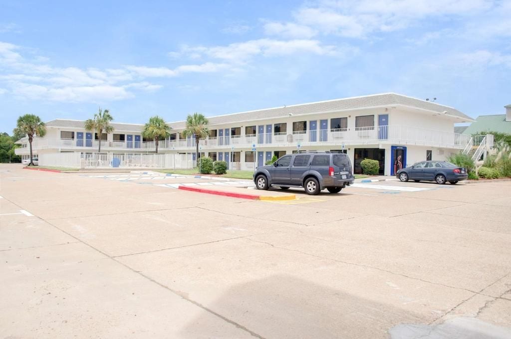 A motel with a two-story structure, a parking lot, and a clear sky.