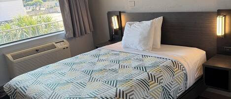 Habitación de hotel moderna con una cama grande, una ventana con cortinas, una mesita de noche con lámpara y un calefactor incorporado.