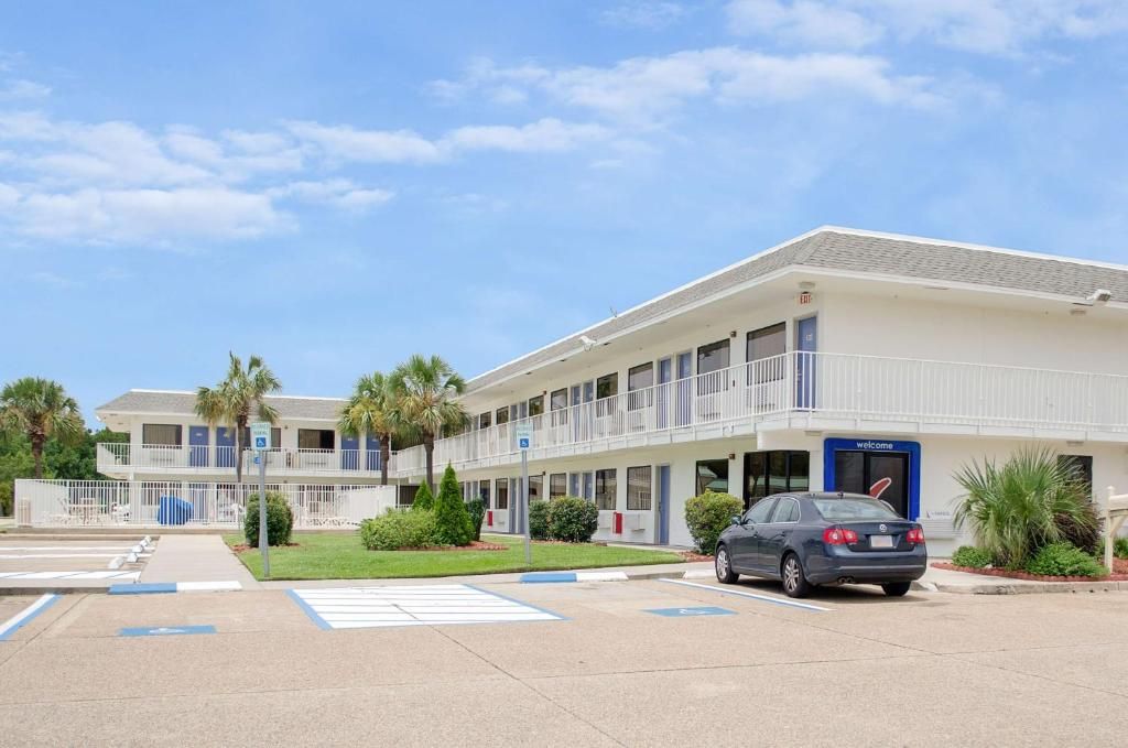 A multi-story motel with a parking lot and a car parked in front.