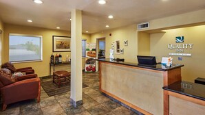 A reception area with a reception desk, leather chairs, a window with a view, and a wall with the Quality Inn logo.