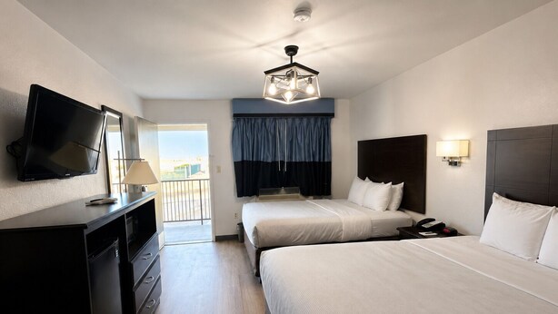 A hotel room with two beds, a TV, a desk, and a balcony.